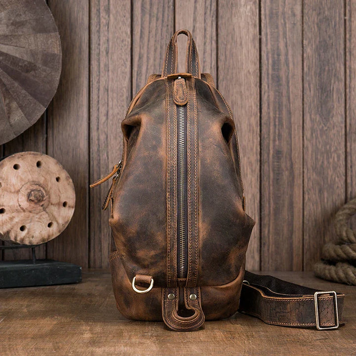 Zaino in pelle vintage marrone con cerniera centrale, stile retrò, su sfondo di legno. Ideale per viaggi e uso quotidiano. Accessorio moda uomo.