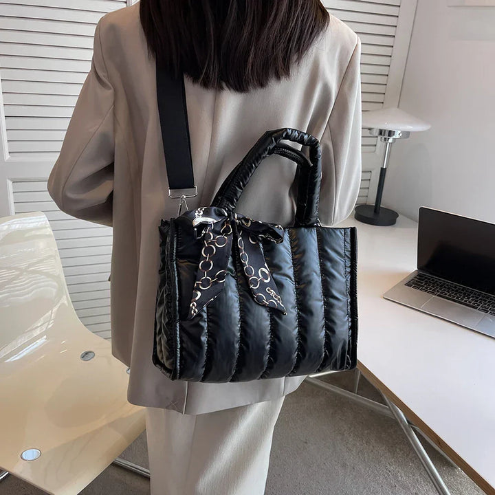 Donna con borsa a tracolla nera imbottita, dettagli a catena, in ufficio moderno. Moda elegante, accessori femminili, stile contemporaneo.
