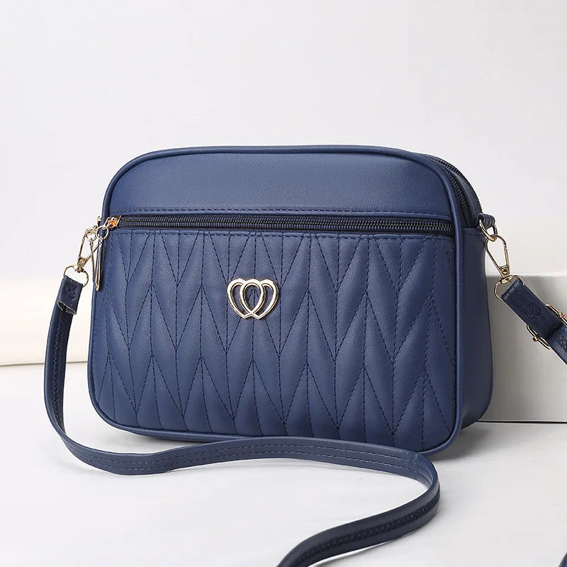 Borsa a tracolla blu in pelle sintetica con motivo trapuntato e decorazione a cuore dorato, ideale per moda donna e accessori eleganti.
