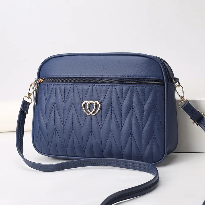 Borsa a tracolla blu in pelle sintetica con motivo trapuntato e decorazione a cuore dorato, ideale per moda donna e accessori eleganti.