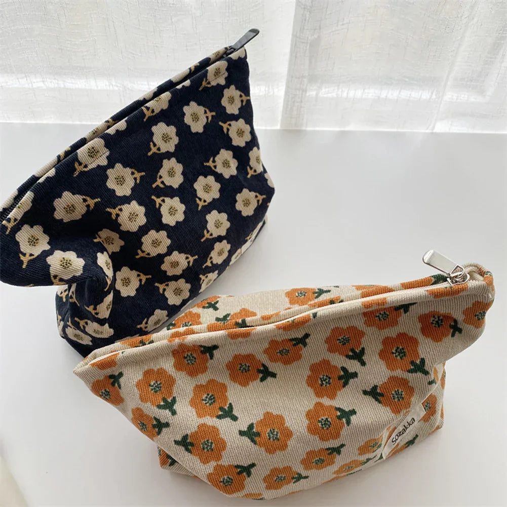 Due astucci in tessuto floreale, uno blu con fiori bianchi e uno beige con fiori arancioni, su sfondo bianco. Accessori moda eleganti e pratici.