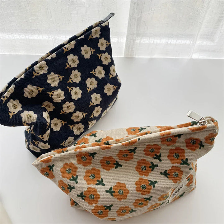 Due astucci in tessuto floreale, uno blu con fiori bianchi e uno beige con fiori arancioni, su sfondo bianco. Accessori moda eleganti e pratici.