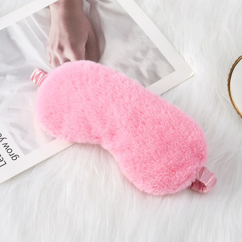 Maschera per dormire rosa in peluche su coperta bianca, accessorio per il sonno, comfort e relax, ideale per viaggi e riposo notturno.