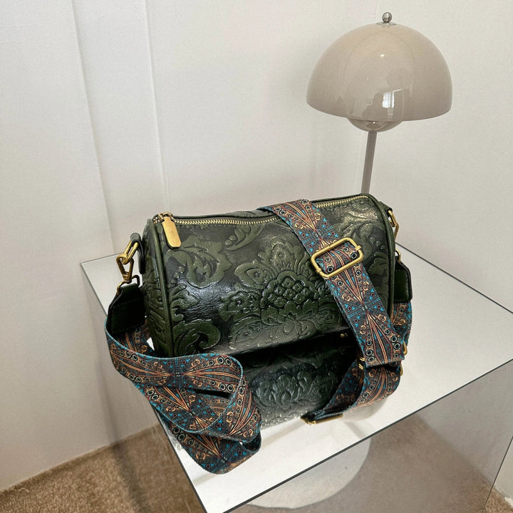Borsa a tracolla verde in pelle con motivo floreale, cinghia regolabile decorata, su tavolo moderno. Accessorio moda elegante e versatile.