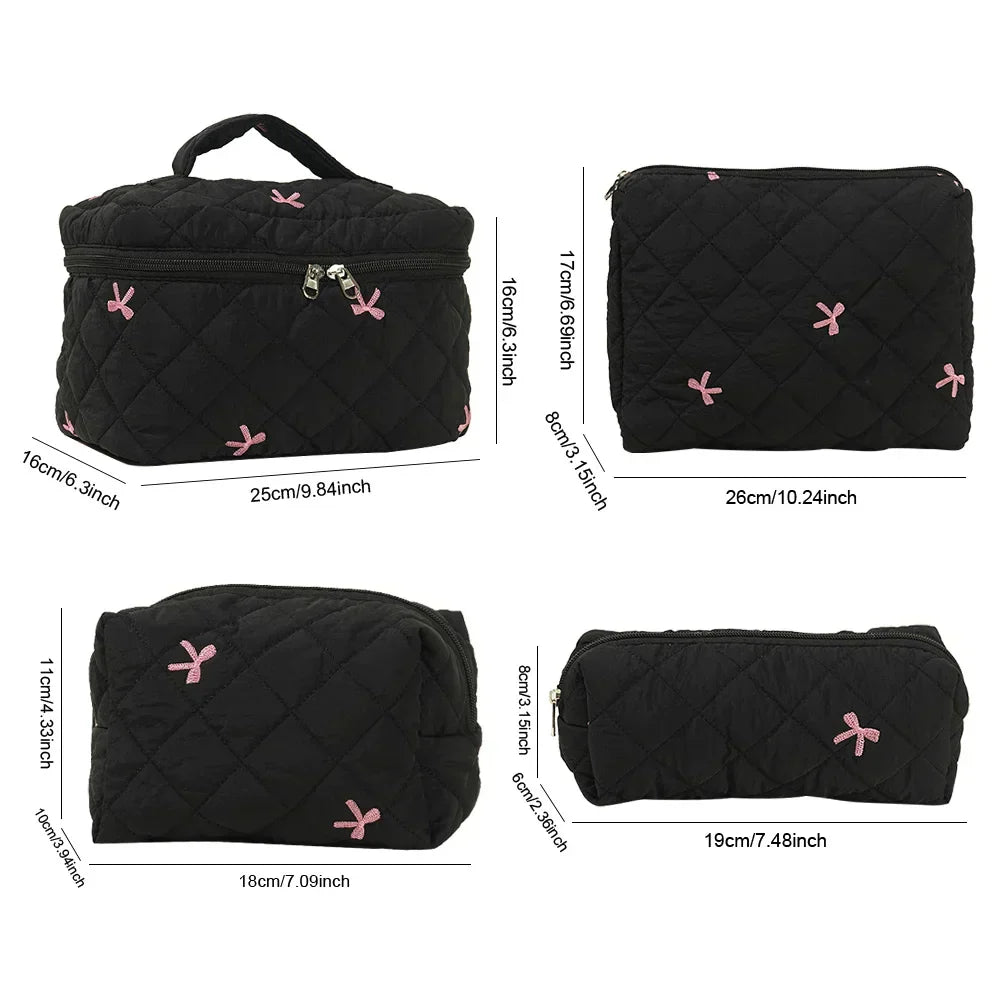 Set di borse da viaggio nere trapuntate con fiocchi rosa, diverse dimensioni, chiusura a zip, ideali per cosmetici e accessori.