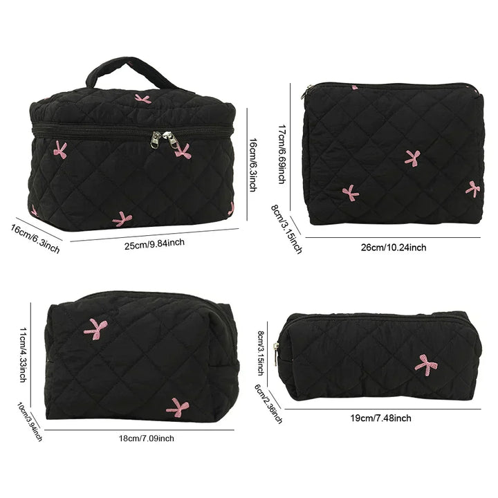 Set di borse da viaggio nere trapuntate con fiocchi rosa, diverse dimensioni, chiusura a zip, ideali per cosmetici e accessori.