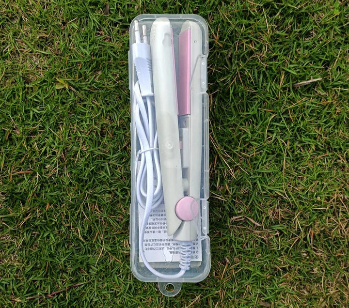 Piastra per capelli portatile bianca e rosa in custodia trasparente su erba verde, con cavo di alimentazione. Accessorio styling compatto e leggero.