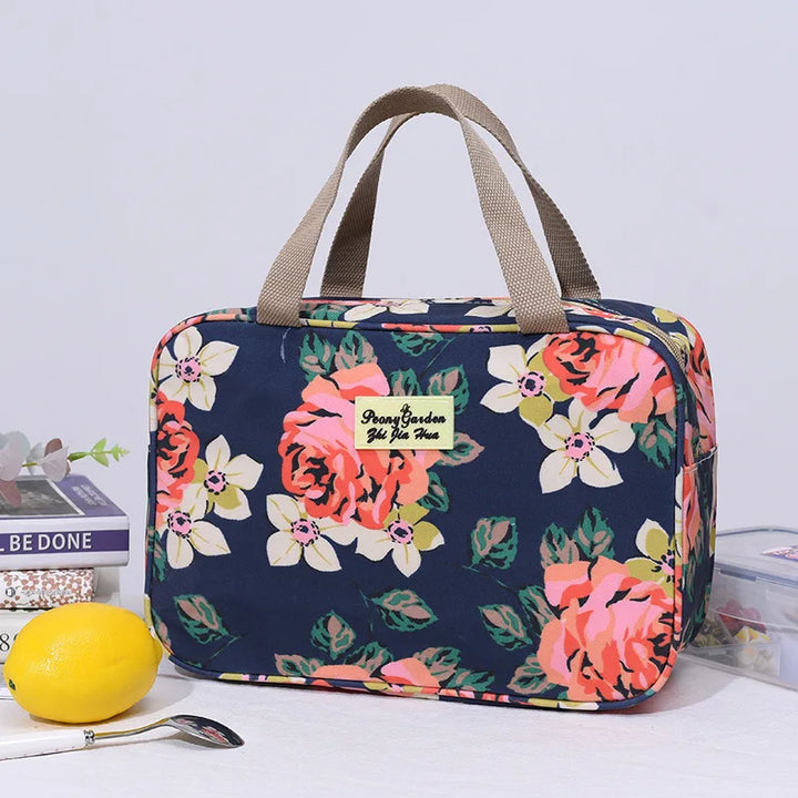 Borsa termica floreale blu con manici beige, ideale per picnic e pranzo al sacco. Design con rose rosa e fiori bianchi. Accessorio pratico e elegante.