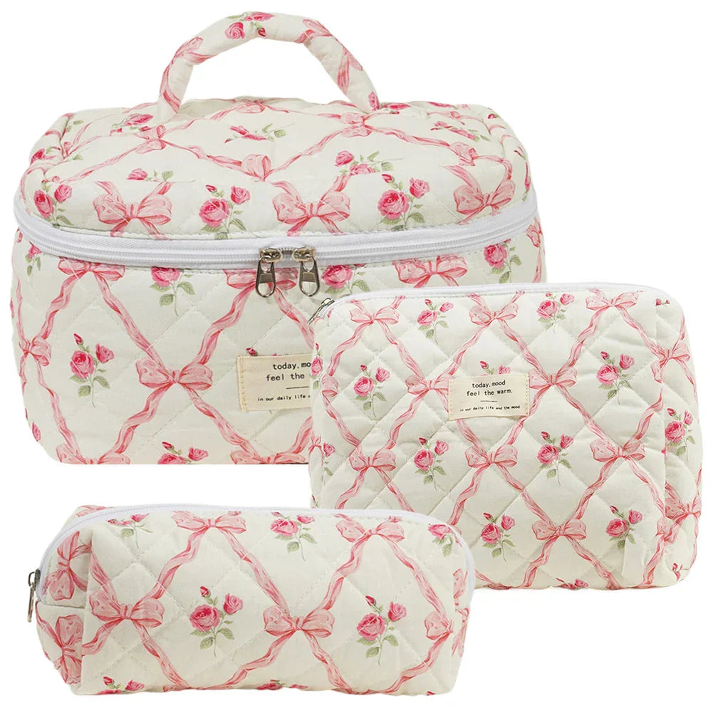 Set di tre beauty case trapuntati bianchi con motivi floreali rosa e fiocchi, chiusura a zip, ideali per viaggi e organizzazione cosmetici.