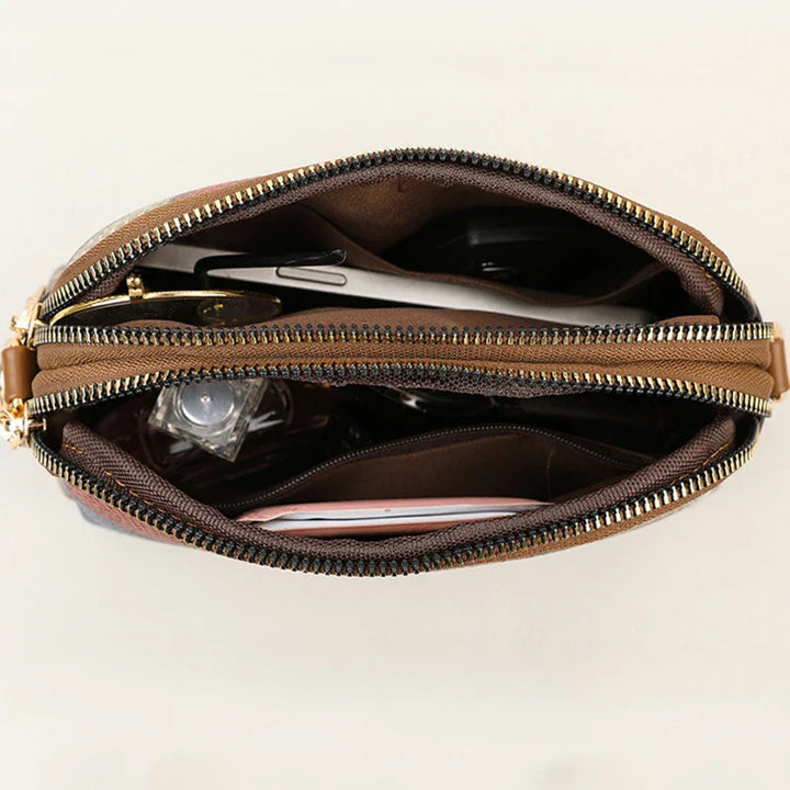 Borsa a tracolla in pelle marrone con cerniera aperta, mostra scomparti interni con smartphone, chiavi e accessori. Design elegante e funzionale.