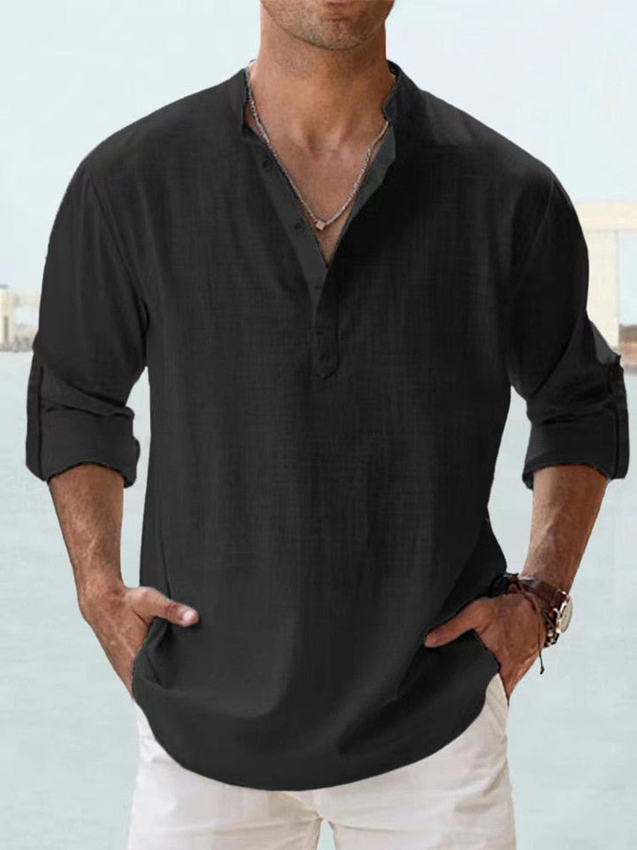 Camicia uomo nera in lino, maniche lunghe arrotolate, colletto alla coreana, abbinata a pantaloni bianchi. Stile casual elegante.