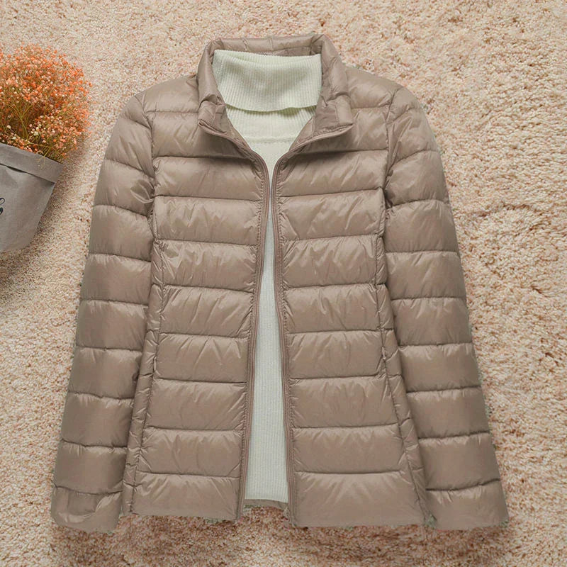 Giacca piumino beige da donna su sfondo chiaro, con maglione bianco a collo alto. Moda invernale, abbigliamento caldo e casual.
