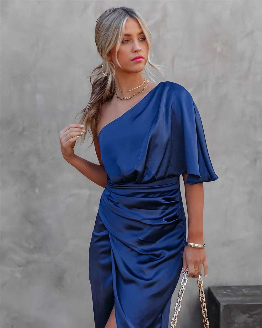 Abito elegante blu in raso monospalla, donna con capelli biondi raccolti, accessori oro, sfondo neutro. Moda femminile, abbigliamento da sera.