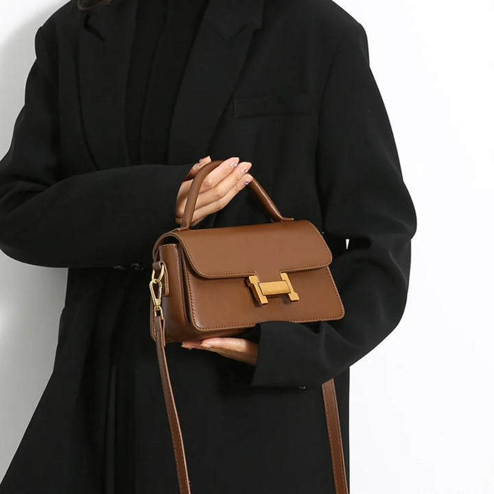Borsa a tracolla marrone in pelle con chiusura dorata, indossata da una persona in cappotto nero. Elegante accessorio moda donna.