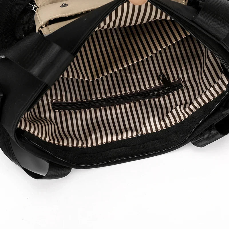 Interno di una borsa nera con fodera a righe bianche e nere, tasca con cerniera. Design elegante, ideale per moda donna e accessori.