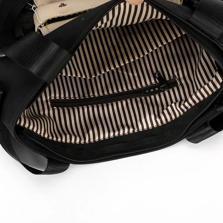 Interno di una borsa nera con fodera a righe bianche e nere, tasca con cerniera. Design elegante, ideale per moda donna e accessori.