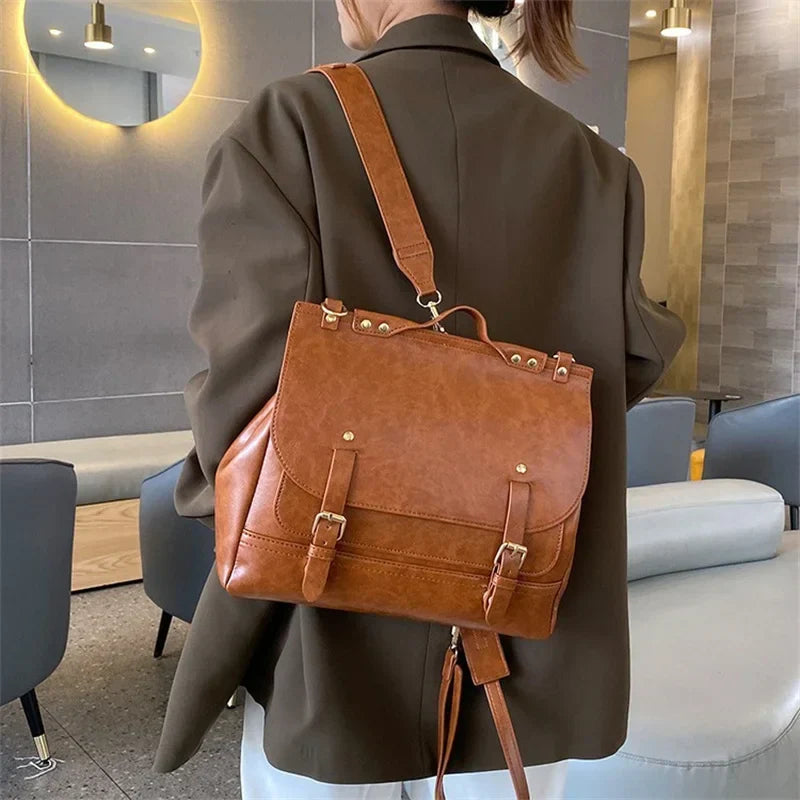 Zaino in pelle marrone elegante, indossato da una persona in giacca scura, in un ambiente moderno. Design con fibbie e dettagli dorati.