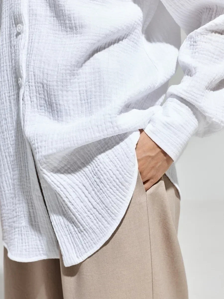 Camicia bianca in cotone a maniche lunghe, tessuto a trama leggera, abbinata a pantaloni beige. Stile casual ed elegante per uomo o donna.