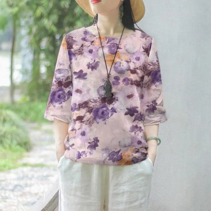 Donna con cappello indossa maglietta floreale viola e pantaloni bianchi, stile casual estivo. Moda donna, abbigliamento estivo, tendenza floreale.