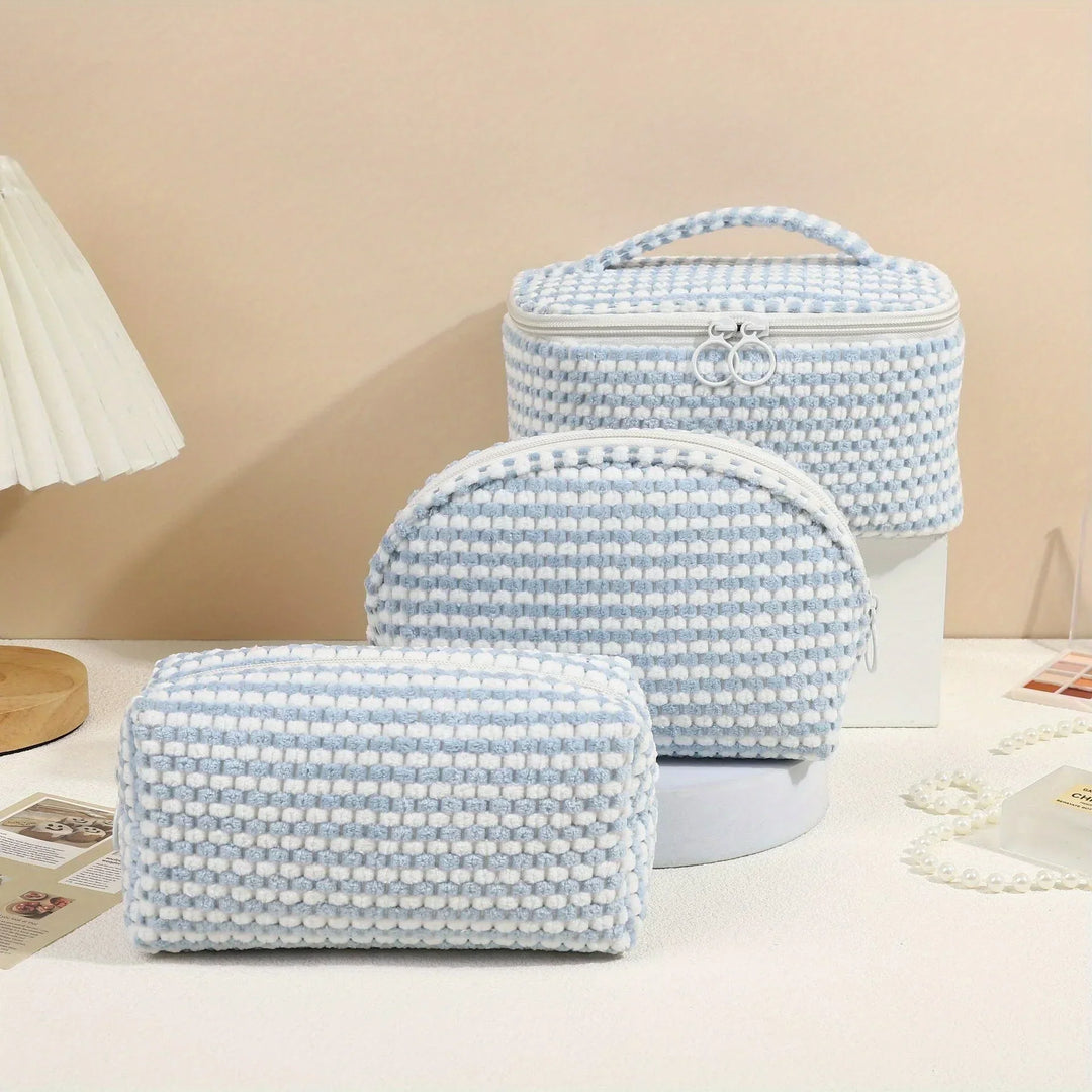 Set di tre borse da toilette in tessuto intrecciato bianco e azzurro, con cerniera e manico, su sfondo beige. Accessori da viaggio eleganti e pratici.