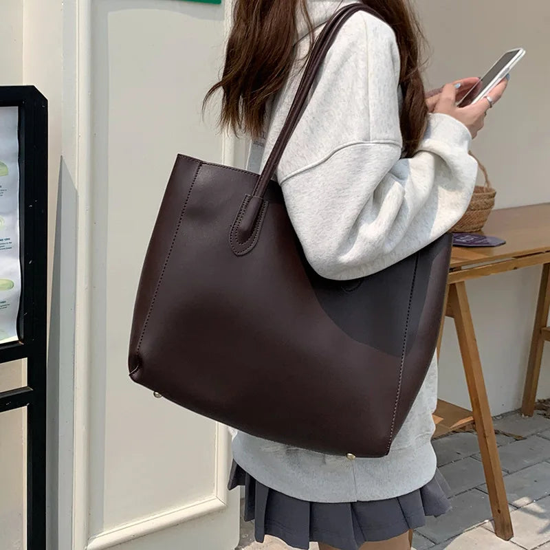Donna con borsa shopper in pelle marrone, indossa felpa grigia e gonna corta. Accessorio moda elegante, ideale per shopping e uso quotidiano.