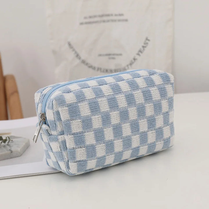 Astuccio a quadri blu e bianchi su tavolo bianco, design elegante e moderno, ideale per cosmetici o accessori, perfetto per viaggi e organizzazione.