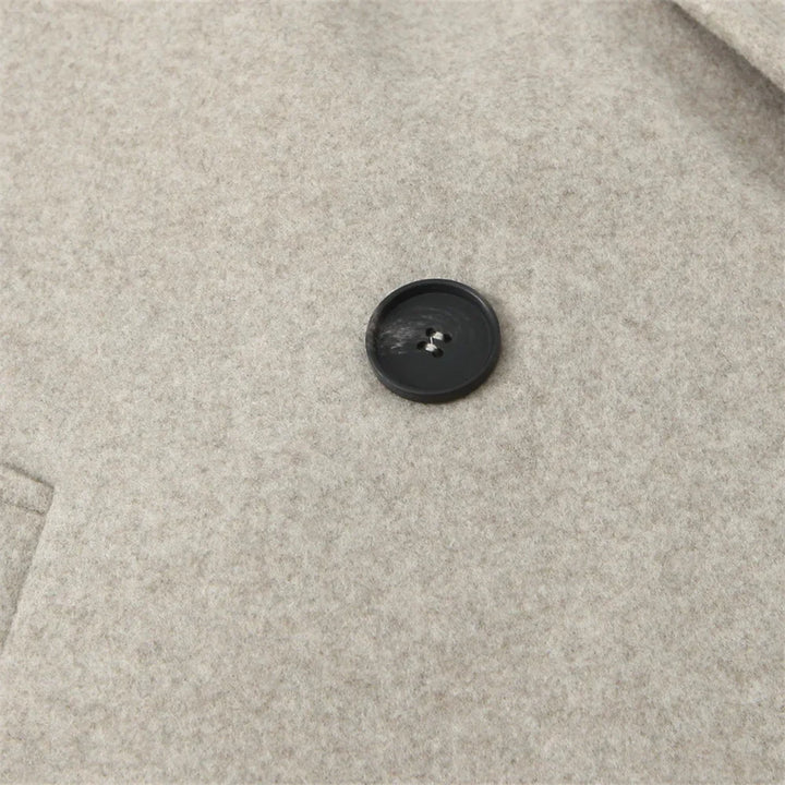 Cappotto in lana beige con bottone nero, tessuto morbido e caldo, ideale per l'inverno. Design elegante e versatile per uomo o donna.
