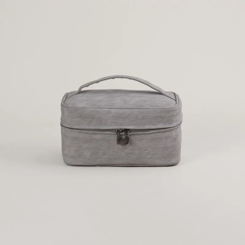 Borsa da viaggio grigia in tessuto, con manico superiore e chiusura a zip. Ideale per organizzare accessori e cosmetici. Design elegante e pratico.