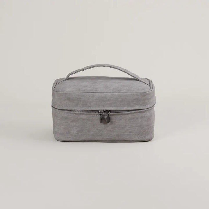 Borsa da viaggio grigia in tessuto, con manico superiore e chiusura a zip. Ideale per organizzare accessori e cosmetici. Design elegante e pratico.