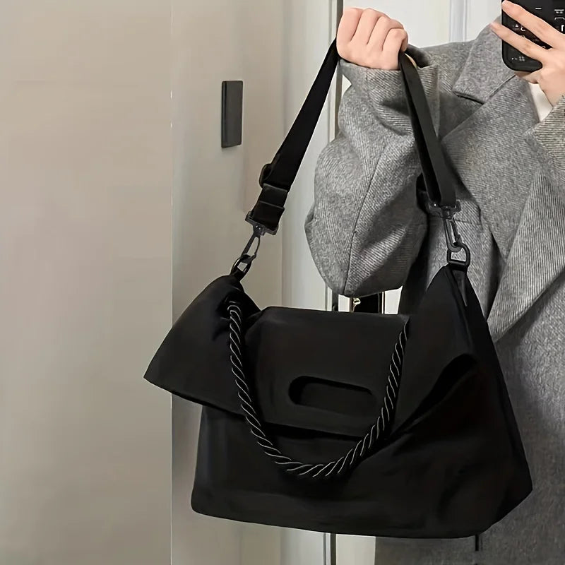 Borsa a tracolla nera elegante, indossata da persona in cappotto grigio. Design moderno, manico intrecciato, ideale per moda urbana.