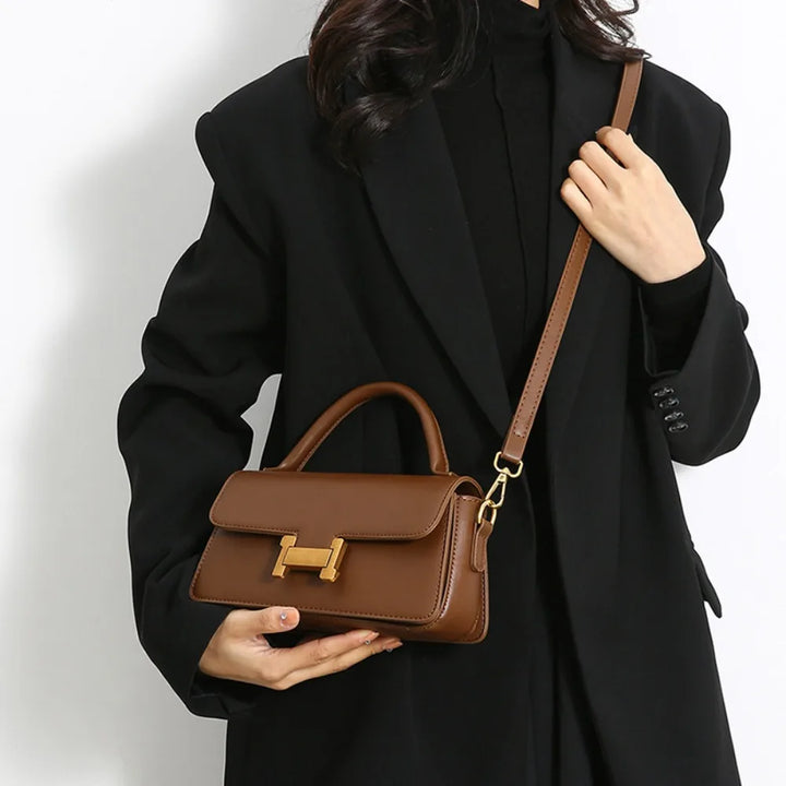Borsa a tracolla marrone in pelle con chiusura dorata, indossata da una donna in cappotto nero. Elegante accessorio moda femminile.