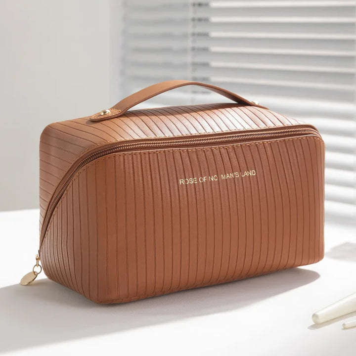 Borsa cosmetica marrone in pelle con cerniera dorata, design a righe, manico superiore, su sfondo bianco. Elegante e pratica per viaggi.