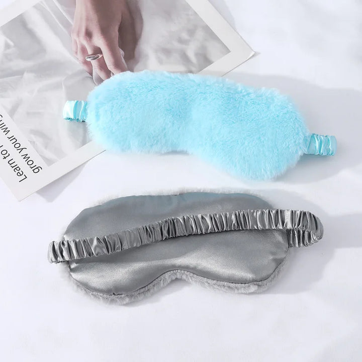 Maschere per dormire in seta e peluche azzurro su lenzuolo bianco. Accessori per il sonno, comfort notturno, relax. Ideali per viaggi e riposo.