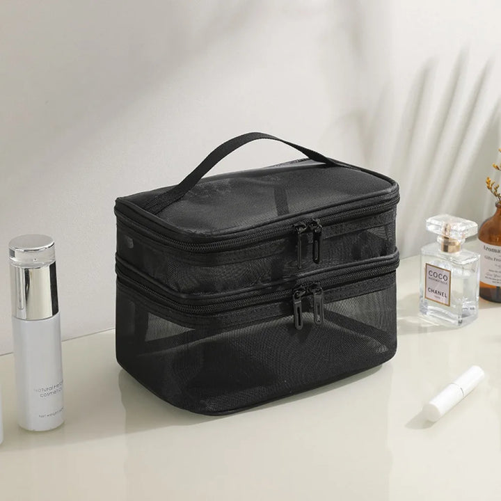 Borsa cosmetica nera a due scomparti con cerniera, su tavolo bianco. Include flaconi di profumo e crema. Ideale per organizzare trucchi e accessori.