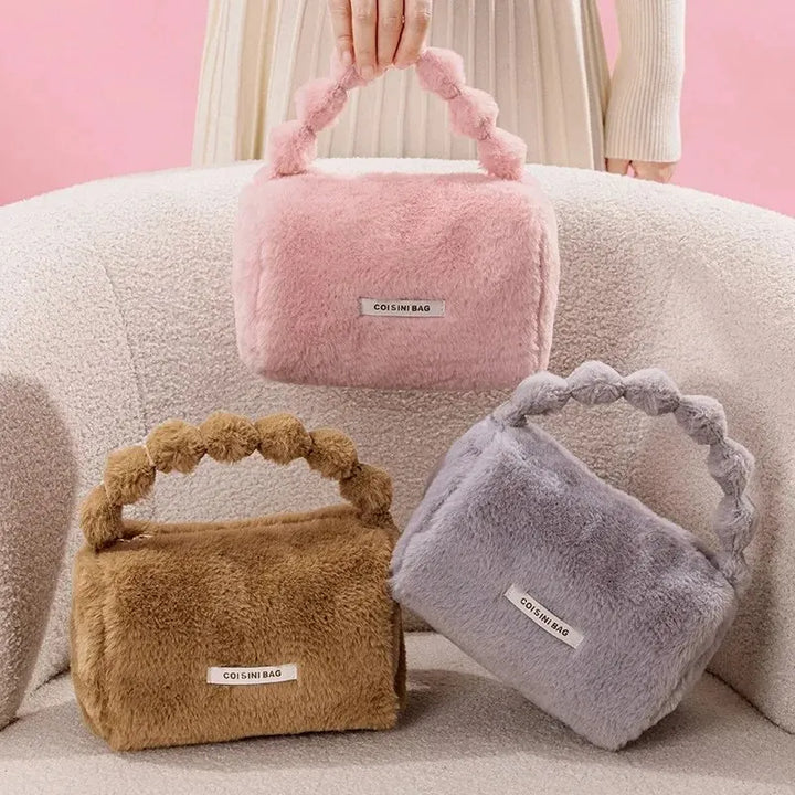 Tre borse in pelliccia sintetica colorate, rosa, marrone e grigio, con manico intrecciato, su sfondo rosa. Eleganti accessori moda invernali.