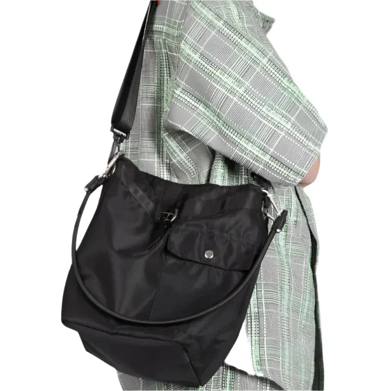 Borsa a tracolla nera in nylon, indossata su camicia a quadri verde e grigia. Design moderno, tasca frontale con bottone, ideale per uso quotidiano.