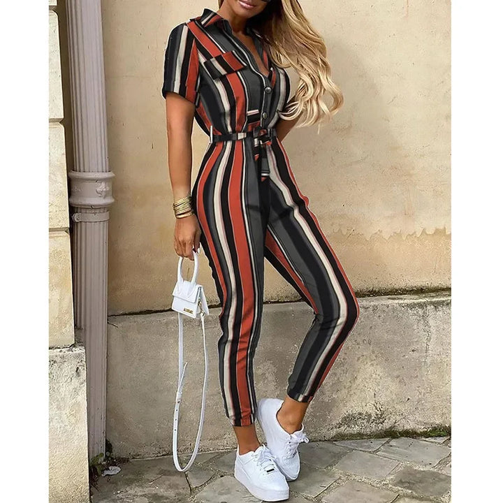 Tuta a righe verticali multicolore, maniche corte, cintura in vita, abbinata a sneakers bianche e borsa a mano bianca. Moda donna casual chic.