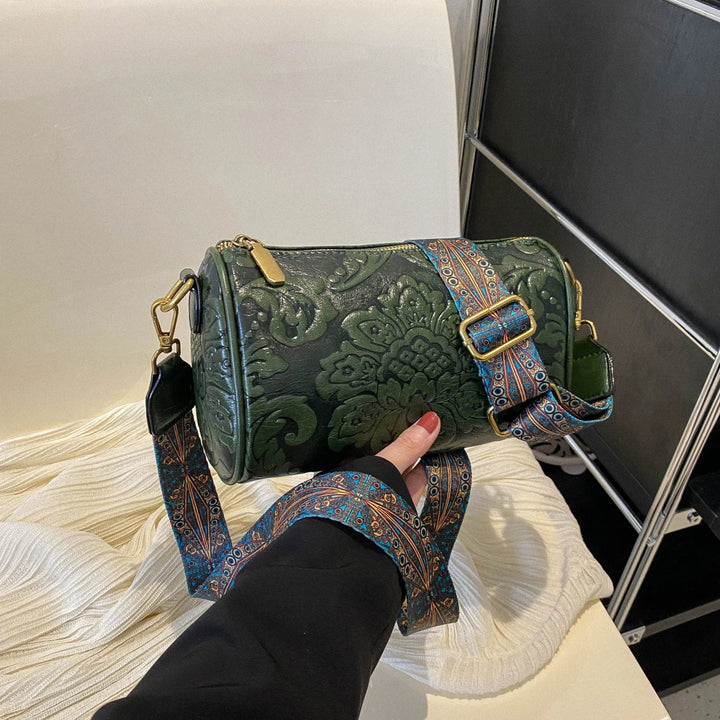 Borsa a tracolla cilindrica verde con motivo floreale in rilievo, cinturino regolabile decorato, chiusura con zip dorata. Accessorio moda elegante.