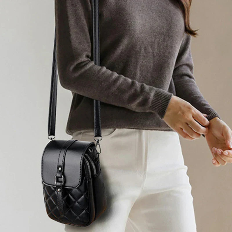 Donna con borsa a tracolla nera in pelle trapuntata, indossa maglione grigio e pantaloni bianchi. Accessorio moda elegante e versatile.