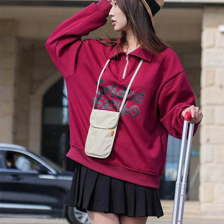 Donna con felpa rossa oversize, gonna nera e cappello di paglia, tiene una valigia. Moda casual autunnale, street style femminile.