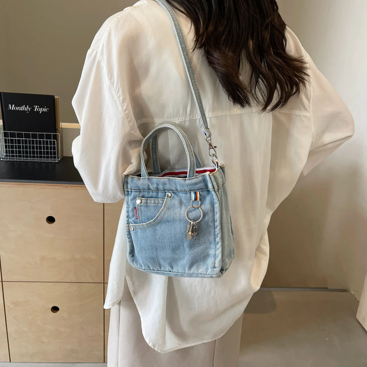 Donna con camicia bianca indossa borsa a tracolla in denim con tasca frontale e portachiavi. Stile casual, moda femminile, accessori trendy.