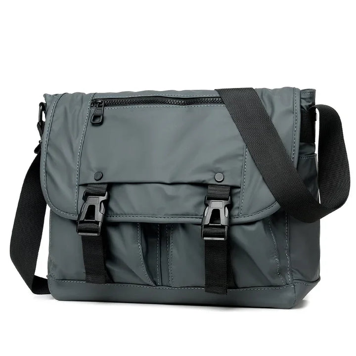 Borsa a tracolla grigia unisex, design moderno, con chiusure a fibbia e tasca frontale con zip. Ideale per lavoro e viaggio.