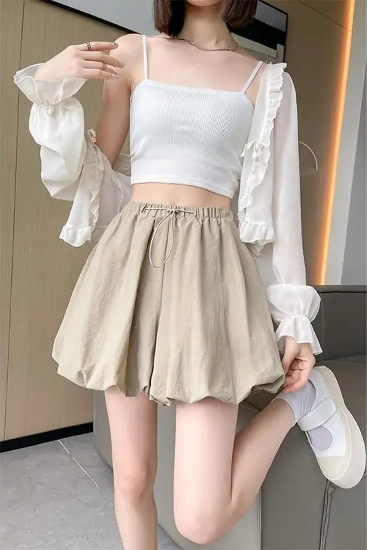 Donna con top bianco e pantaloncini beige, posa moderna. Moda estiva casual, abbigliamento femminile trendy, outfit leggero e confortevole.