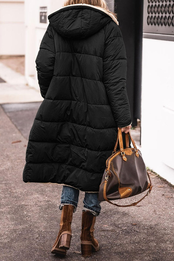 Donna con cappotto lungo nero imbottito, borsa in pelle marrone, stivali invernali, strada urbana. Moda invernale, abbigliamento caldo, stile casual.