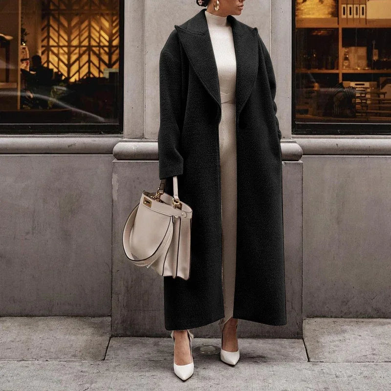 Cappotto lungo nero elegante donna, abbinato a borsa beige e scarpe bianche, moda autunno inverno, look sofisticato urbano.