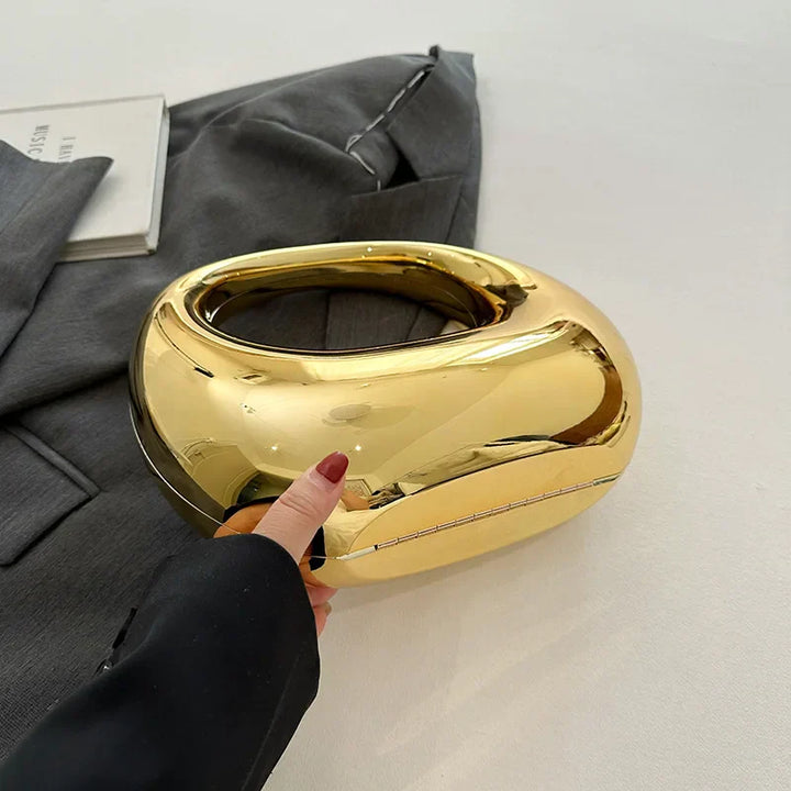 Borsa a mano dorata lucida su sfondo grigio, design moderno e elegante, accessorio moda femminile, perfetta per eventi e serate glamour.