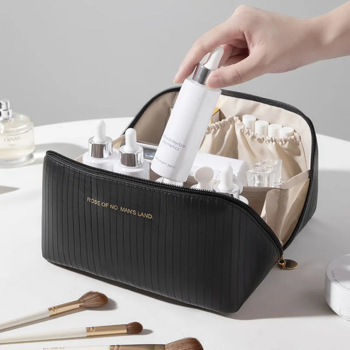 Astuccio cosmetico nero con flaconi di siero e pennelli da trucco su tavolo bianco. Organizzatore da viaggio elegante e funzionale per prodotti di bellezza.