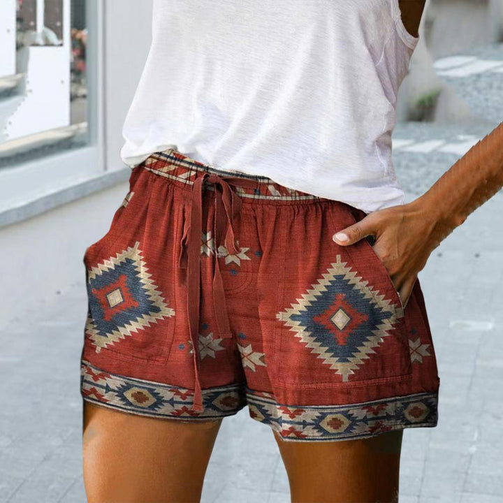 Shorts donna etnici rossi con tasche, motivo geometrico tribale, indossati con top bianco. Moda estiva casual, abbigliamento femminile trendy.