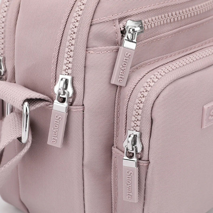 Zaino rosa in tessuto resistente con cerniere multiple e dettagli in metallo argentato, ideale per moda femminile e viaggi.