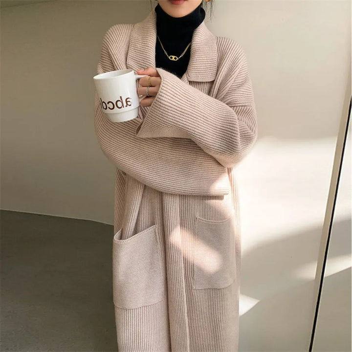 Cappotto lungo beige in maglia a coste, tasche frontali, indossato su dolcevita nero. Stile casual elegante, perfetto per l'autunno inverno.